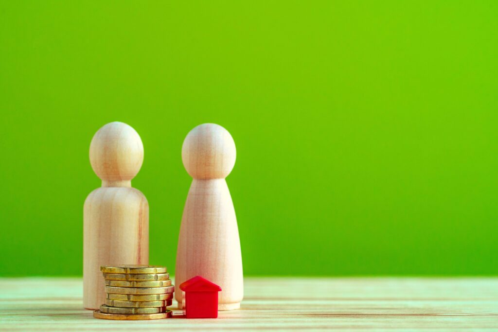 Wooden family with toy house and stack of coins close up